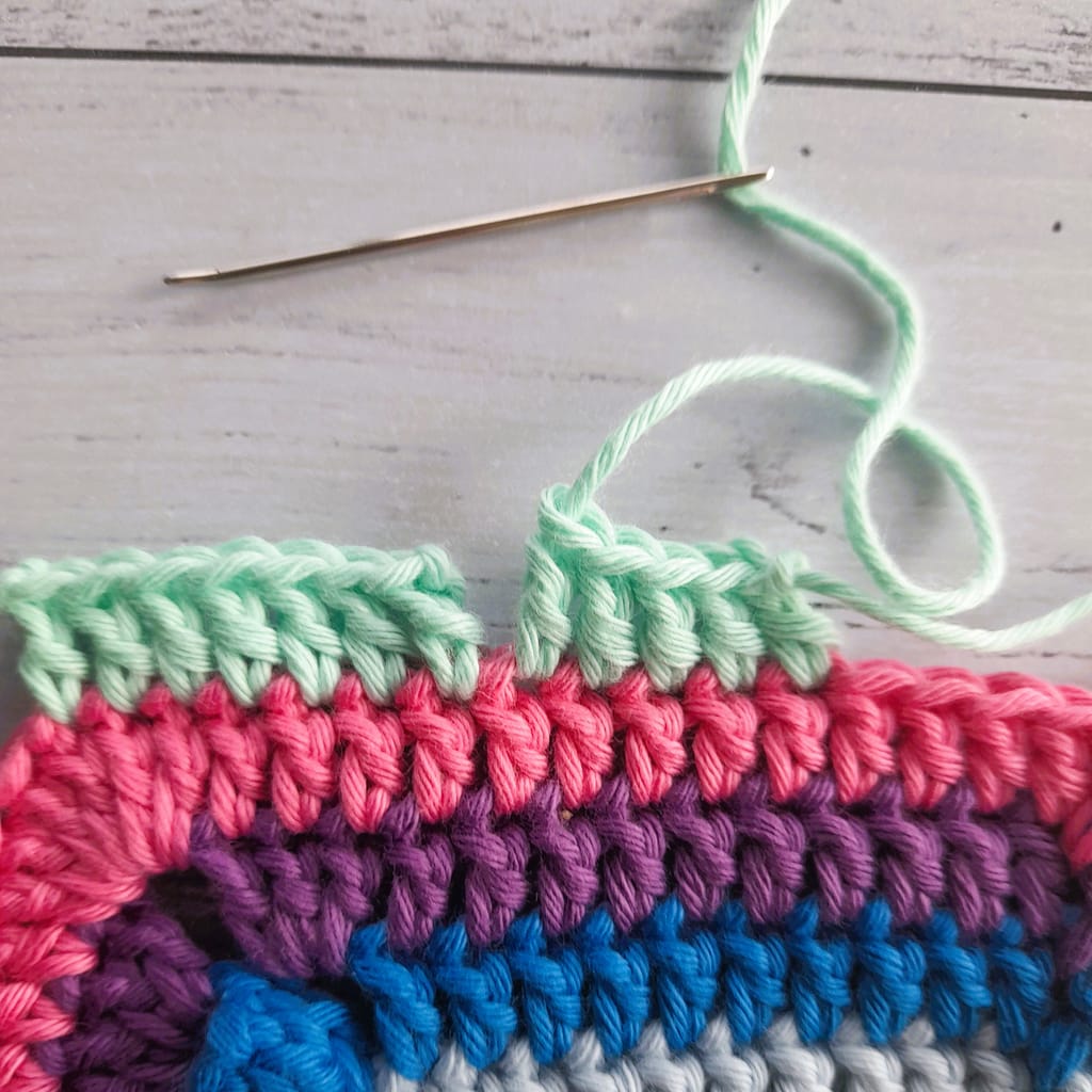 striped piece of crochet fabric with tapestry needle threaded in preparation for making an invisible join