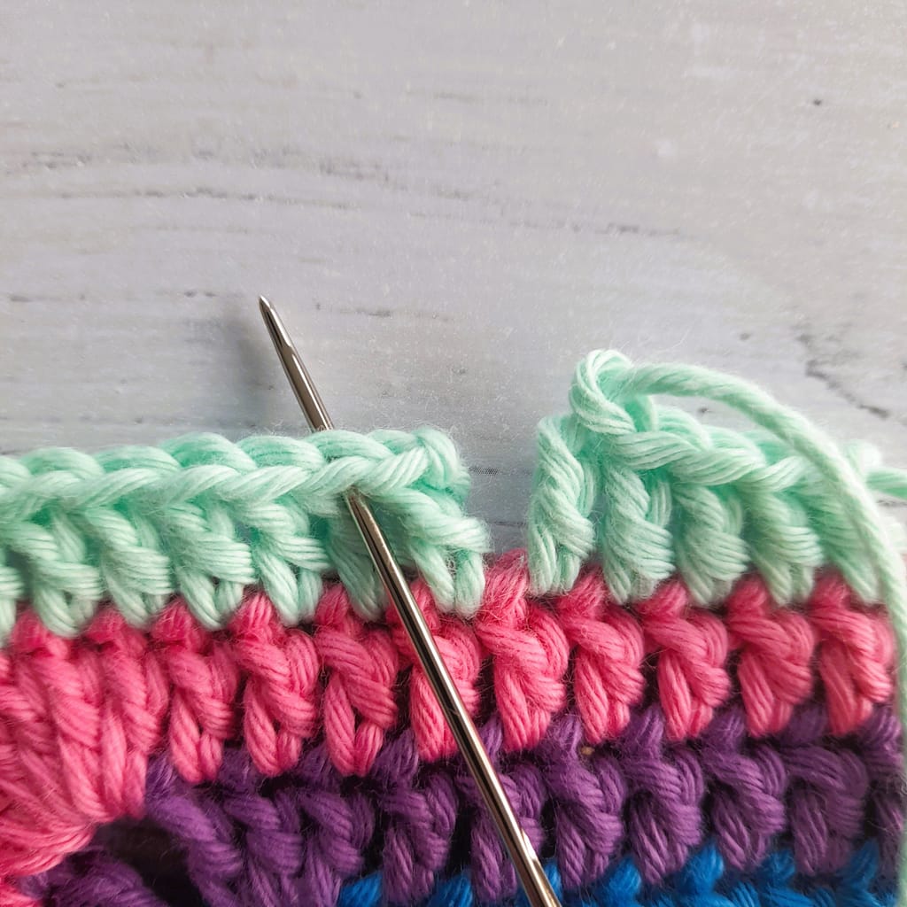 striped crochet fabric with tapestry needle inserted during making of an invisible join
