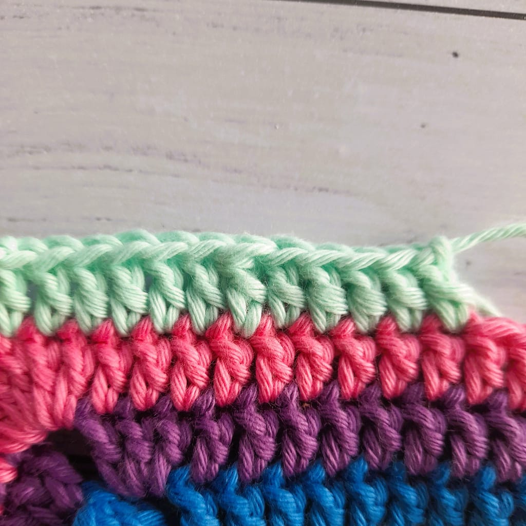 striped crochet fabric closeup in blue, purple, coral and mint green yarn