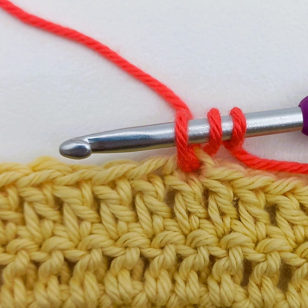 close up of yellow crochet fabric with red crochet stitches in it