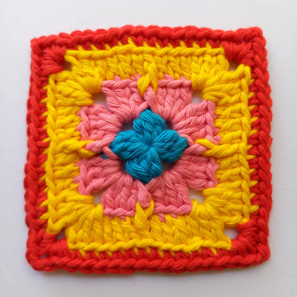 A small crochet granny square with a variety of stitches and in 4 colours of yarn - blue, pink, yellow and red