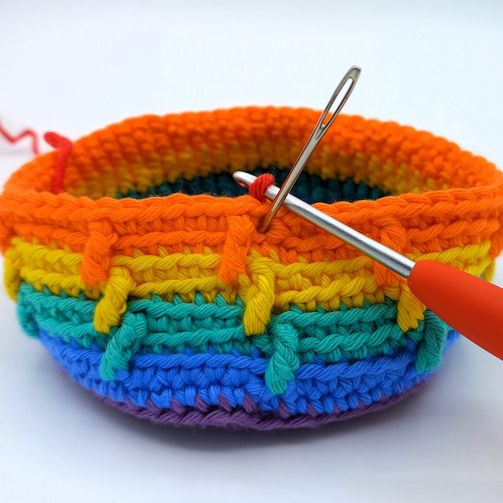 rainbow crochet basked in progress with darning needle showing placement of next stitch