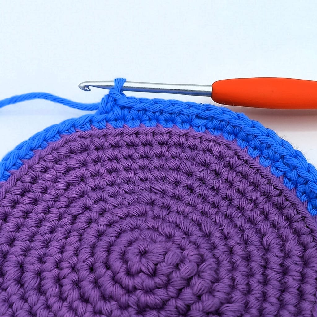 purple crochet circle with colour change to blue yarn in progress by orange crochet hook