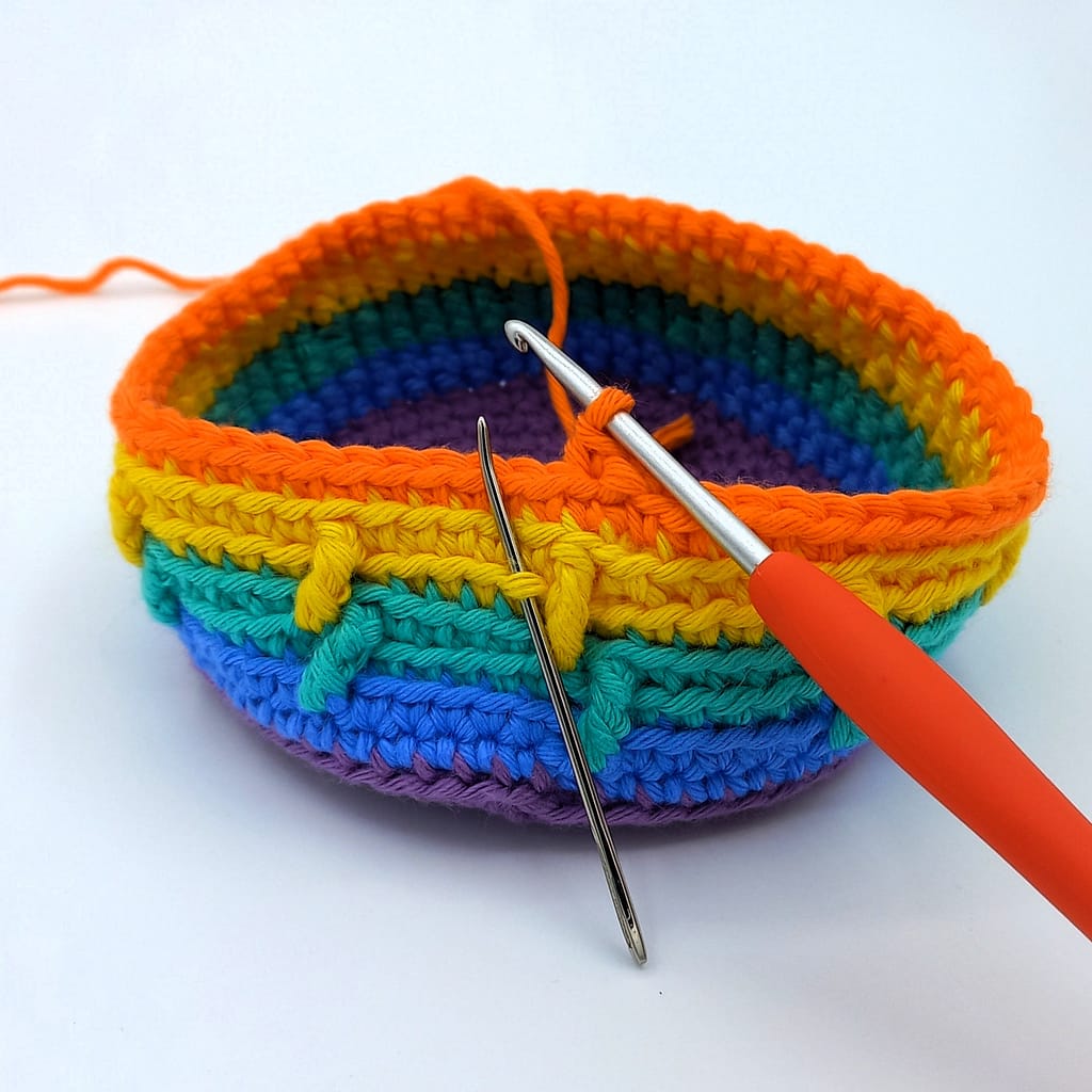 rainbow crochet blanket in progress, rainbow colours, yarn needle showing placement of next stitch