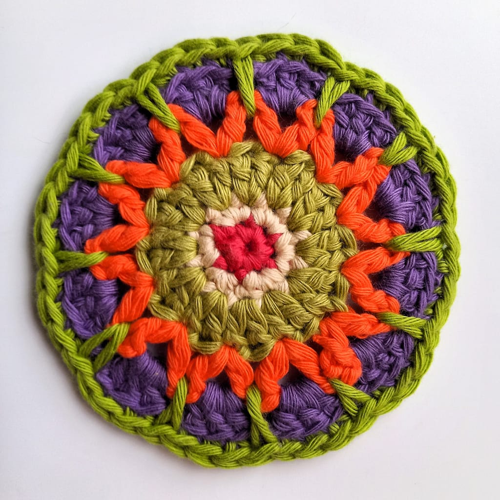 single crochet spike stitches in green on outer round of a crochet mandala