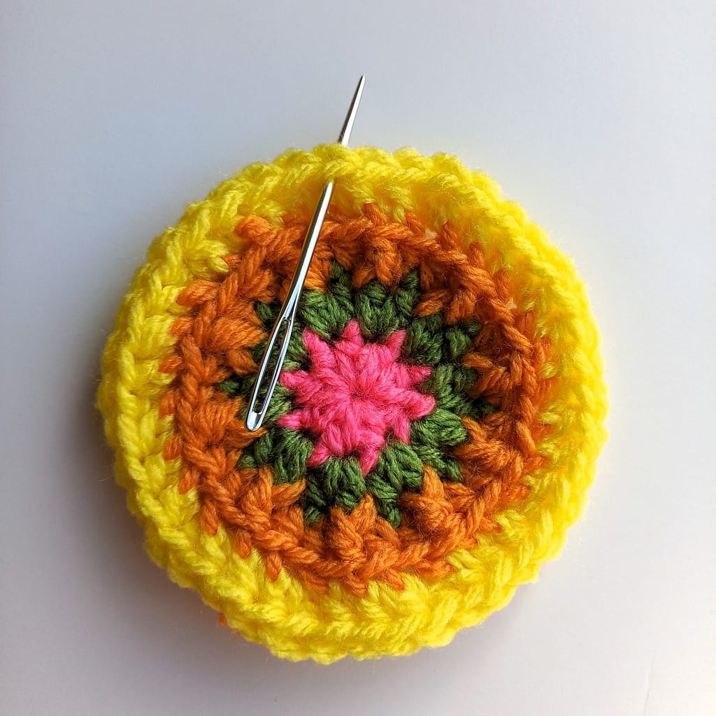 a small crochet circle in different colours with a darning needle showing the placement of the next stitch