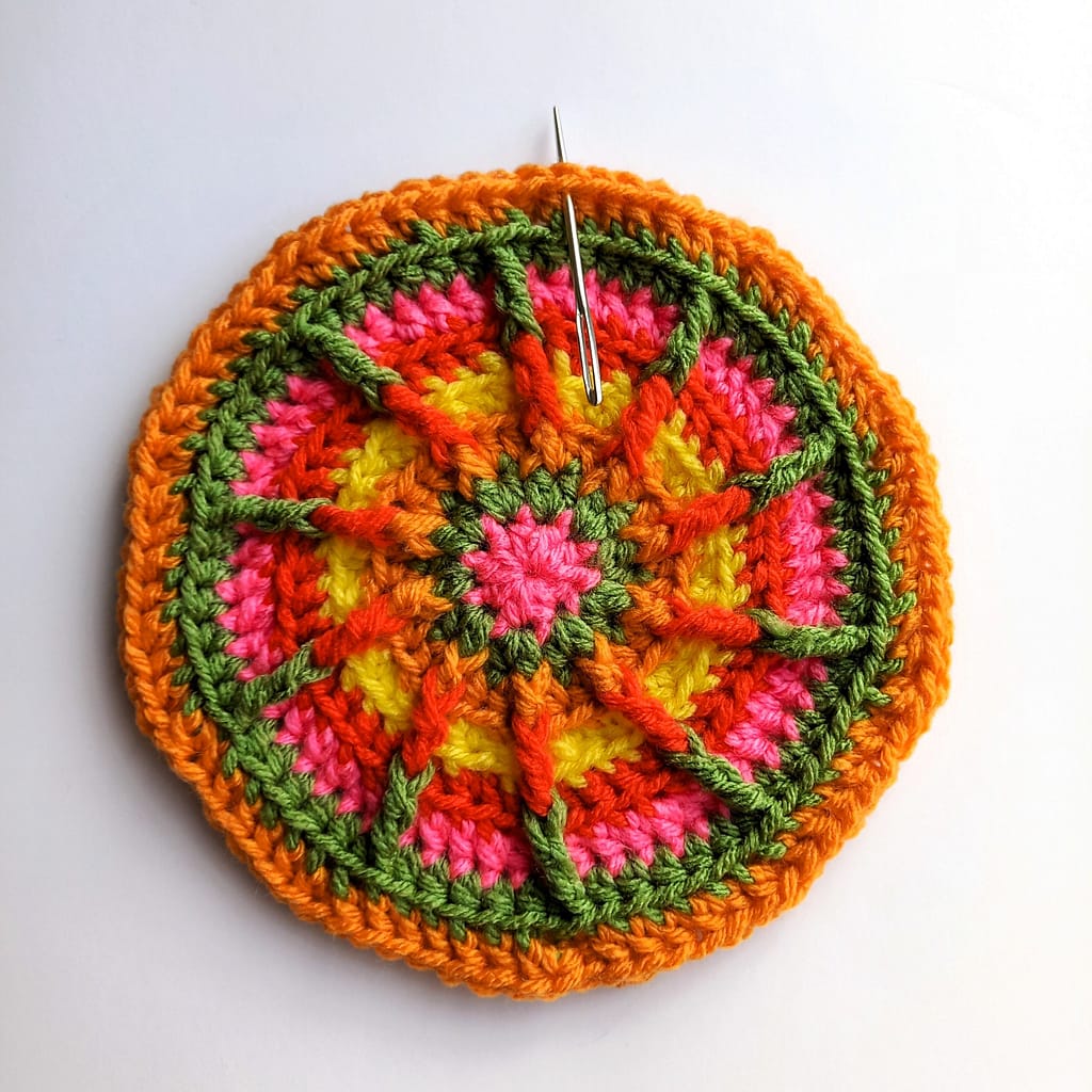 a crocheted circle in multiple colours with a darning needle indicating the placement of the first stitch in the next round