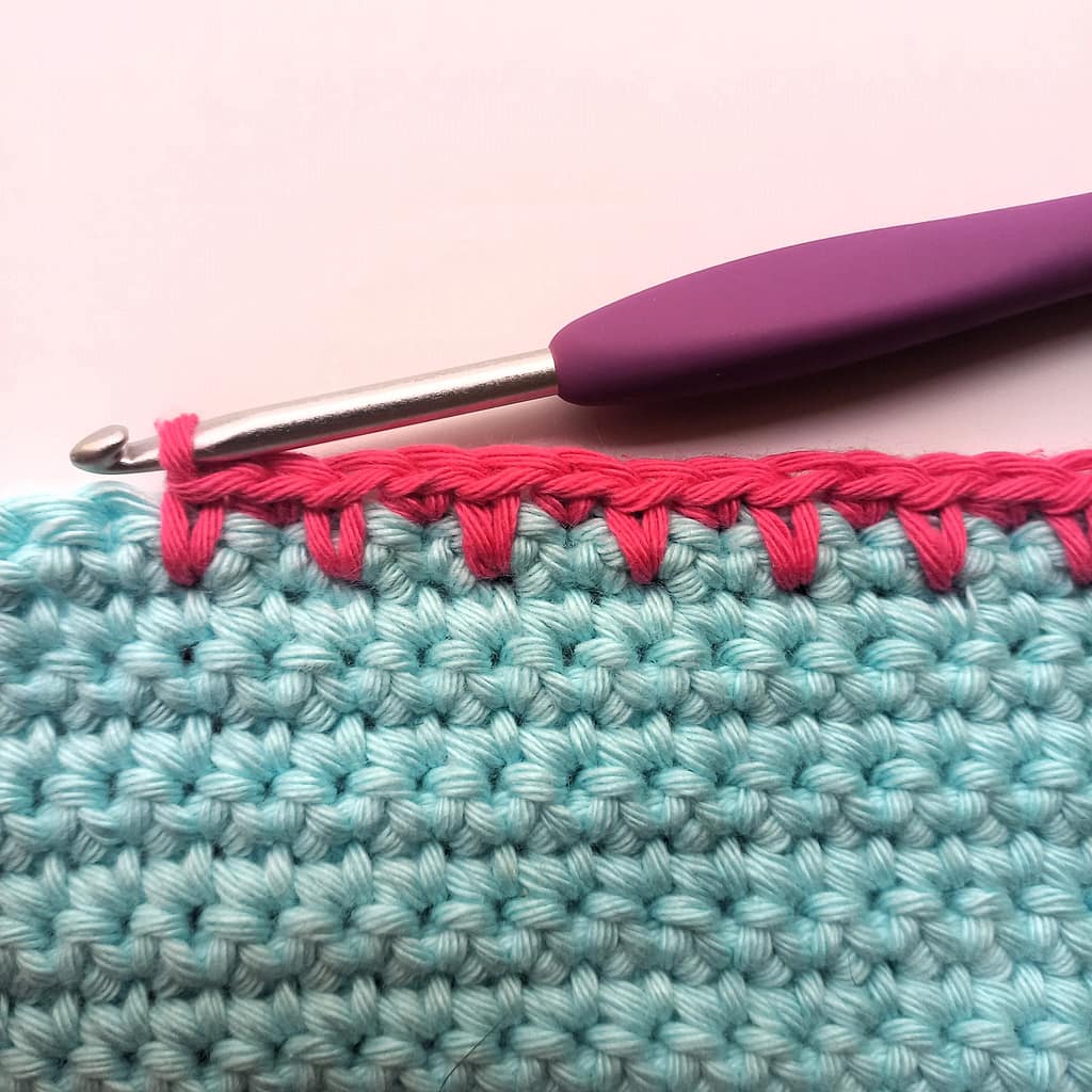 a row of pink single crochet spike stitch on a blue crochet fabric