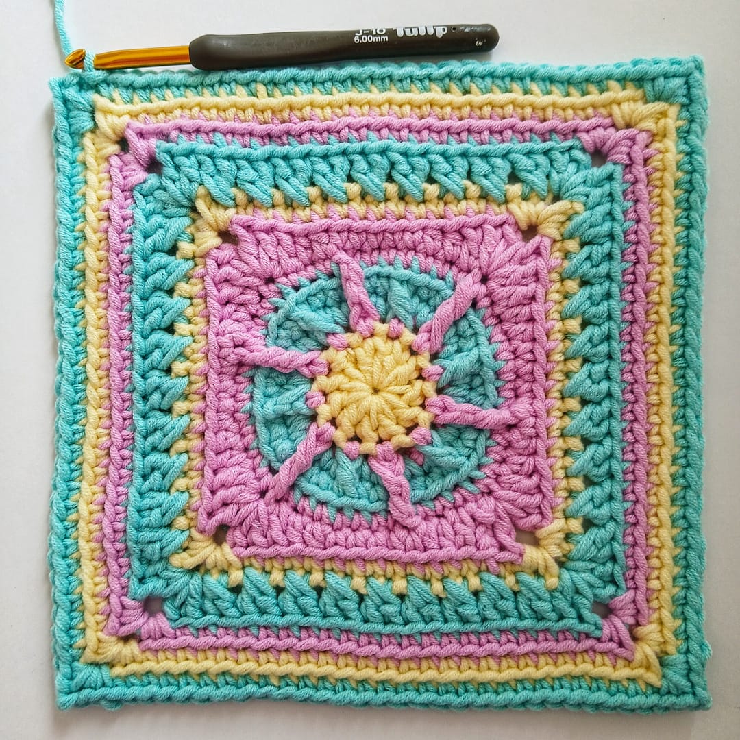 Crochet granny square in alternating pink, blue and yellow yarns, here shown at round 11 of the written instructions that accompany the images