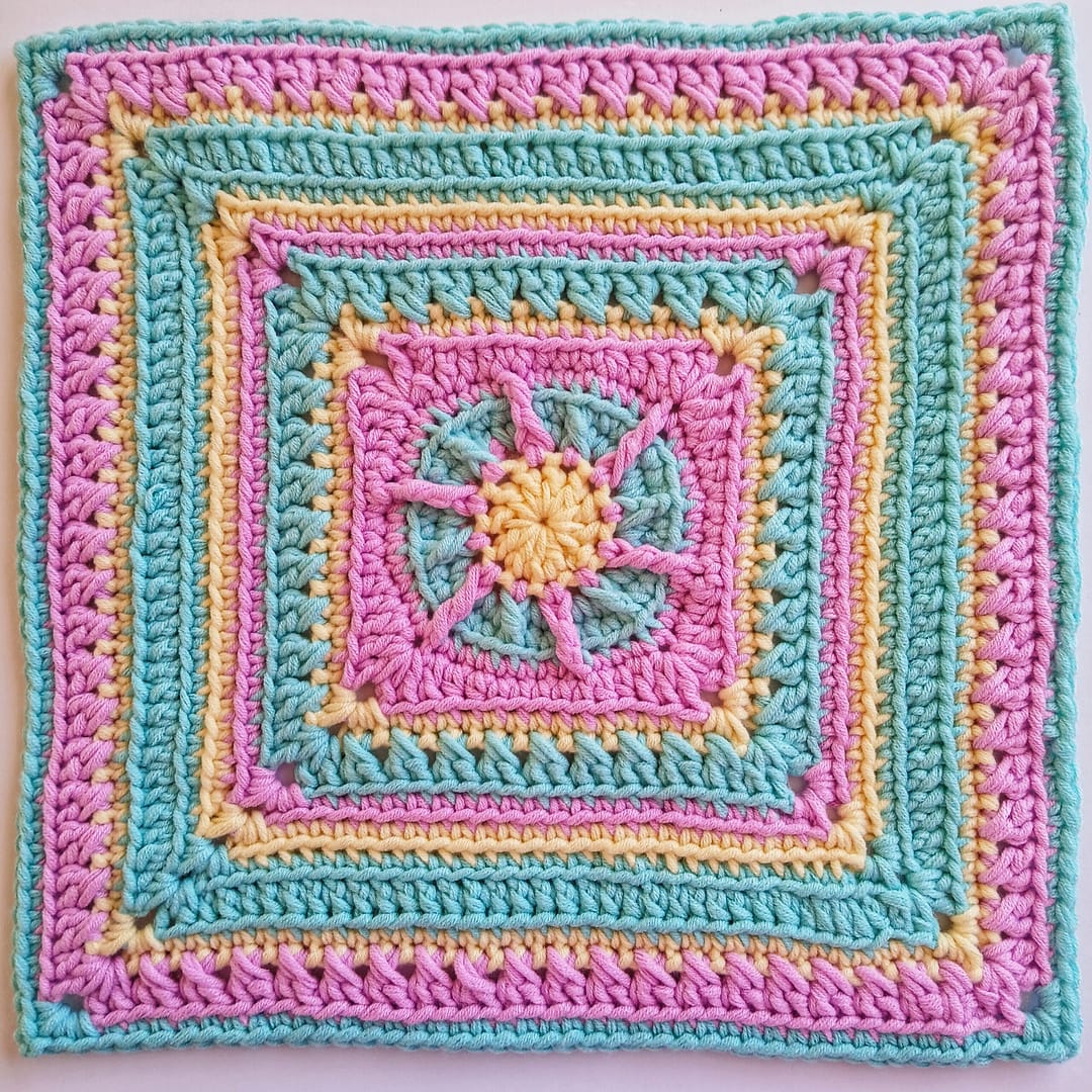 The completed Equinox granny square in close up, all rounds completed in alternating blue, yellow and pink yarns