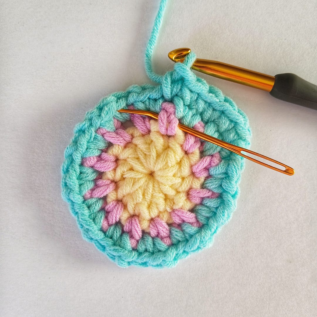 Round 4 of the crochet pattern in progress with a needle showing the placement of the FPdc in the round 2 single crochet