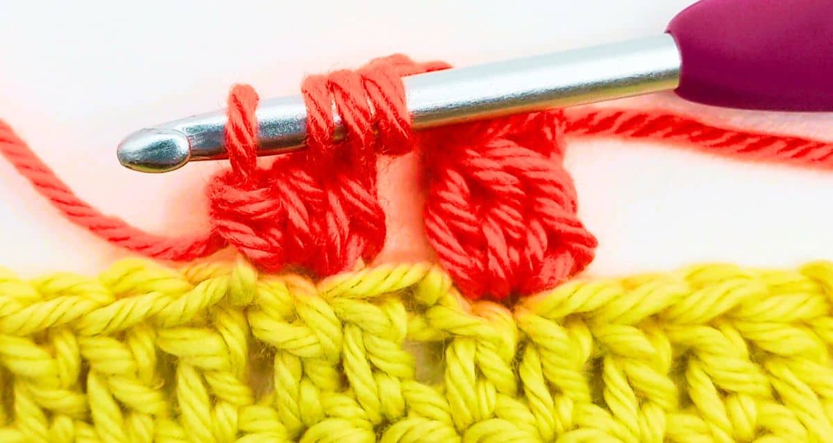 red crochet bobble stitches in progress on a yellow crochet fabric