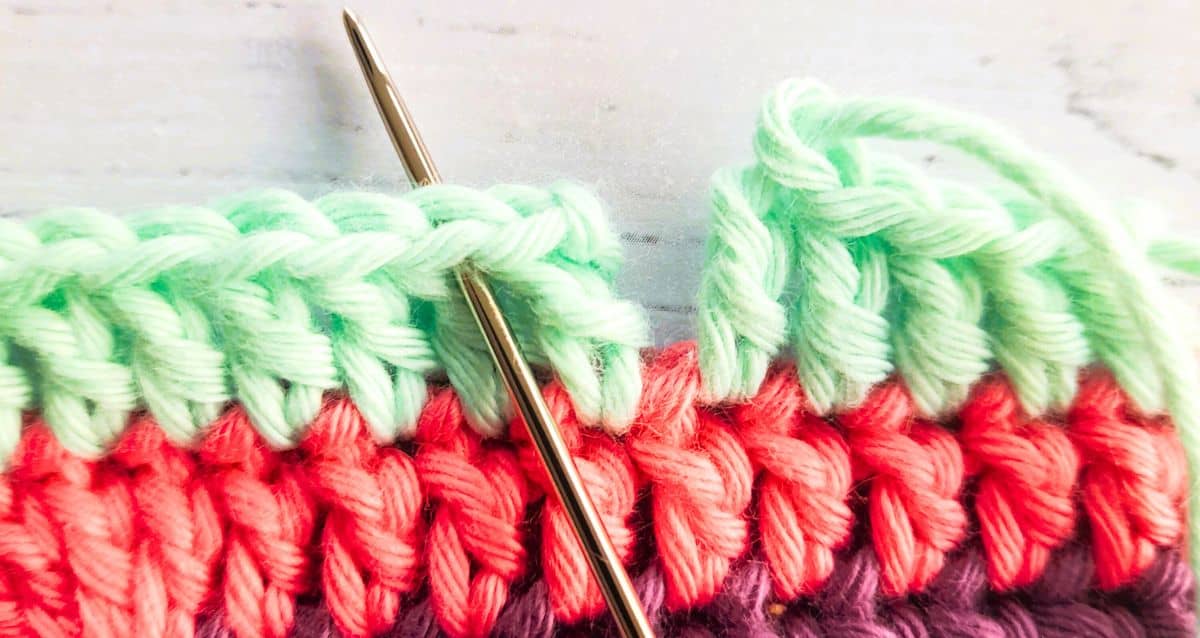 closeup of striped crochet fabric with tapestry needle inserted to complete an invisible join