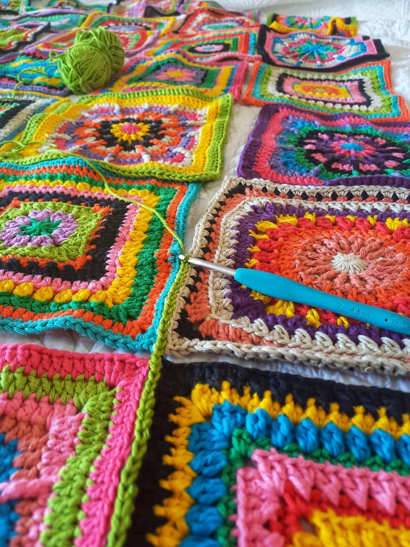 colourful crochet granny squares being joined with a blue crochet hook