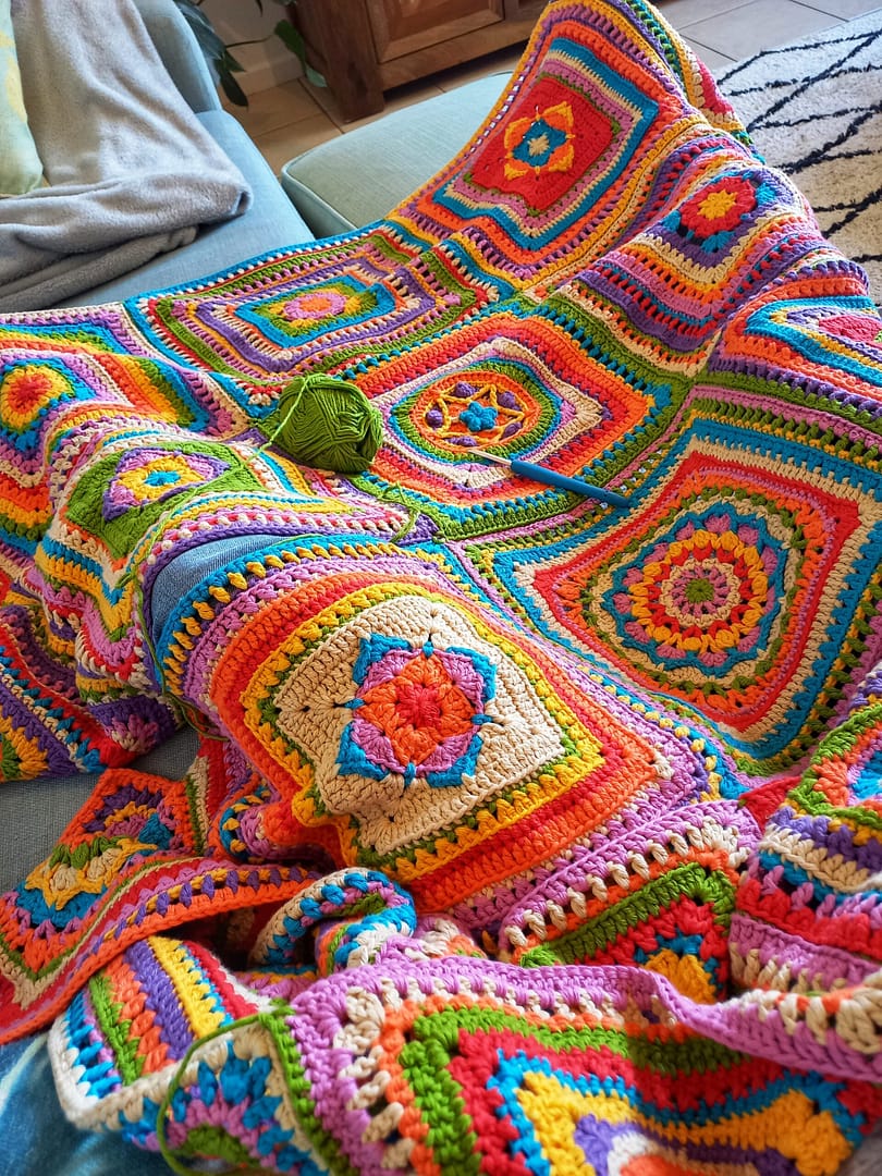 very brightly coloured crochet blanket with a crochet hook and ball of yarn on top