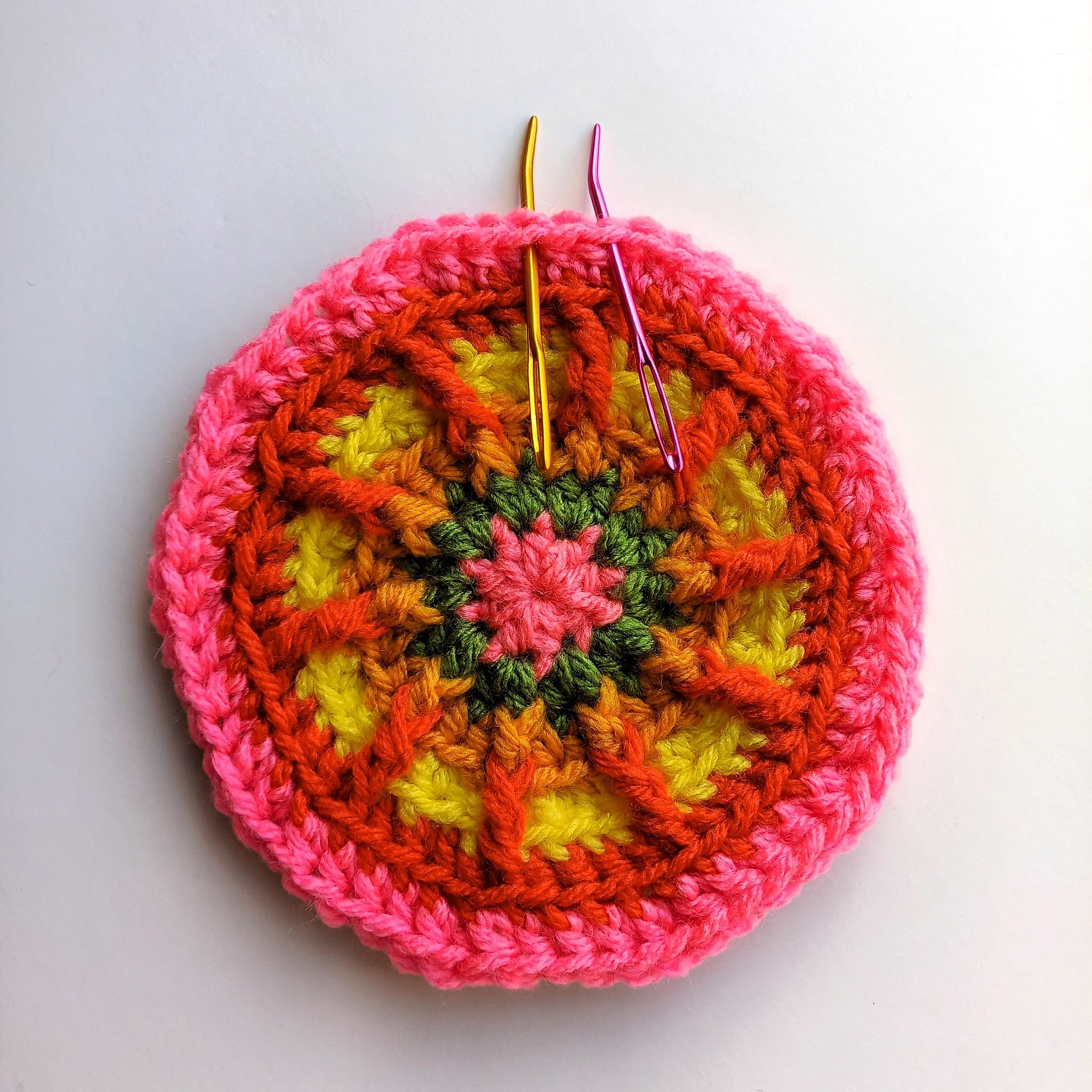 a crochet circles in multiple colours with 2 different coloured yarn needles indicating the placement of the stitches in the next round